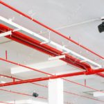 Fire spriانظمة الرش الالىnkler system with red pipes is placed to hanging from the ceiling inside of an unfinished new building.