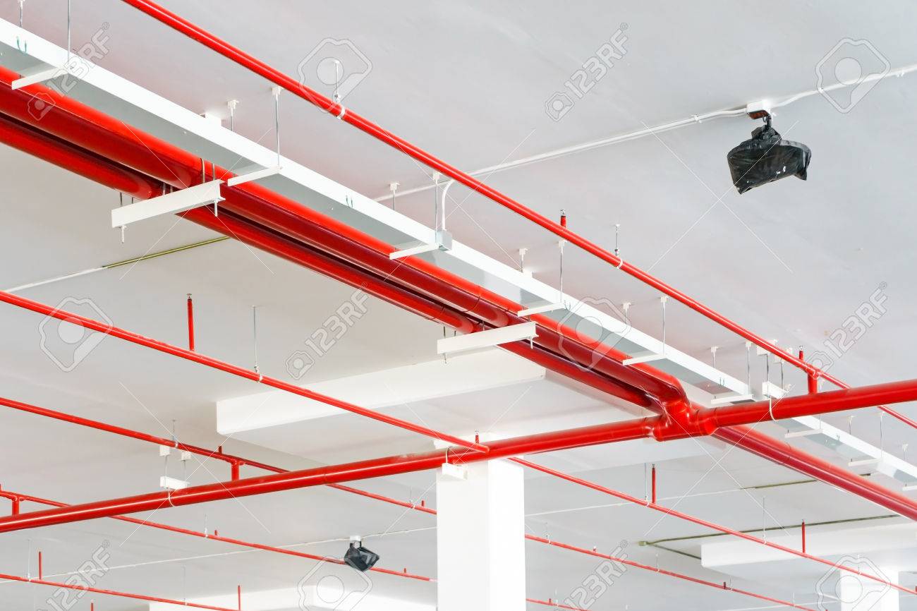 Fire spriانظمة الرش الالىnkler system with red pipes is placed to hanging from the ceiling inside of an unfinished new building.